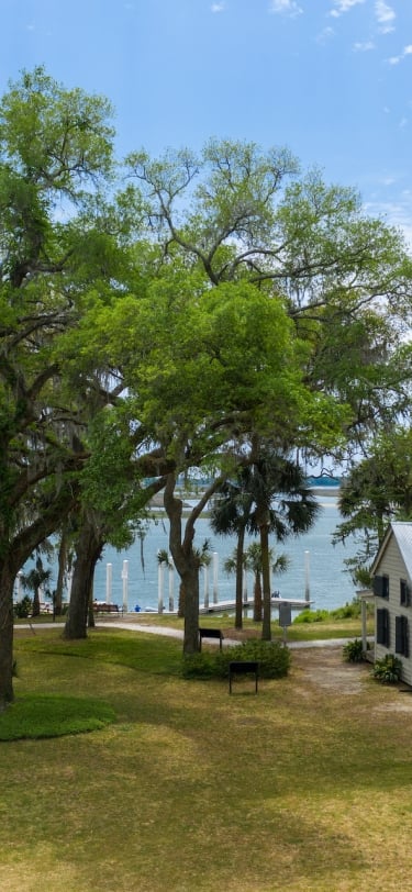 white house with large trees and water in the distance