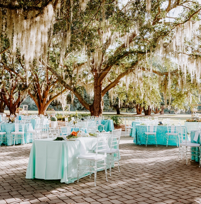 tables set for an elegant outdoor event in Riders Courtyard at Hewitt Oaks, surrounded by a canopy of live oak trees